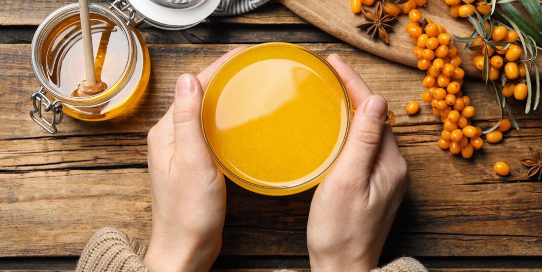 Woman,With,Cup,Of,Fresh,Sea,Buckthorn,Tea,At,Wooden